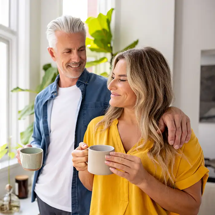 man and woman smiling together and holding cups in living room