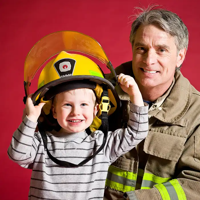firefighter smiling with boy wearing firefighter helmet